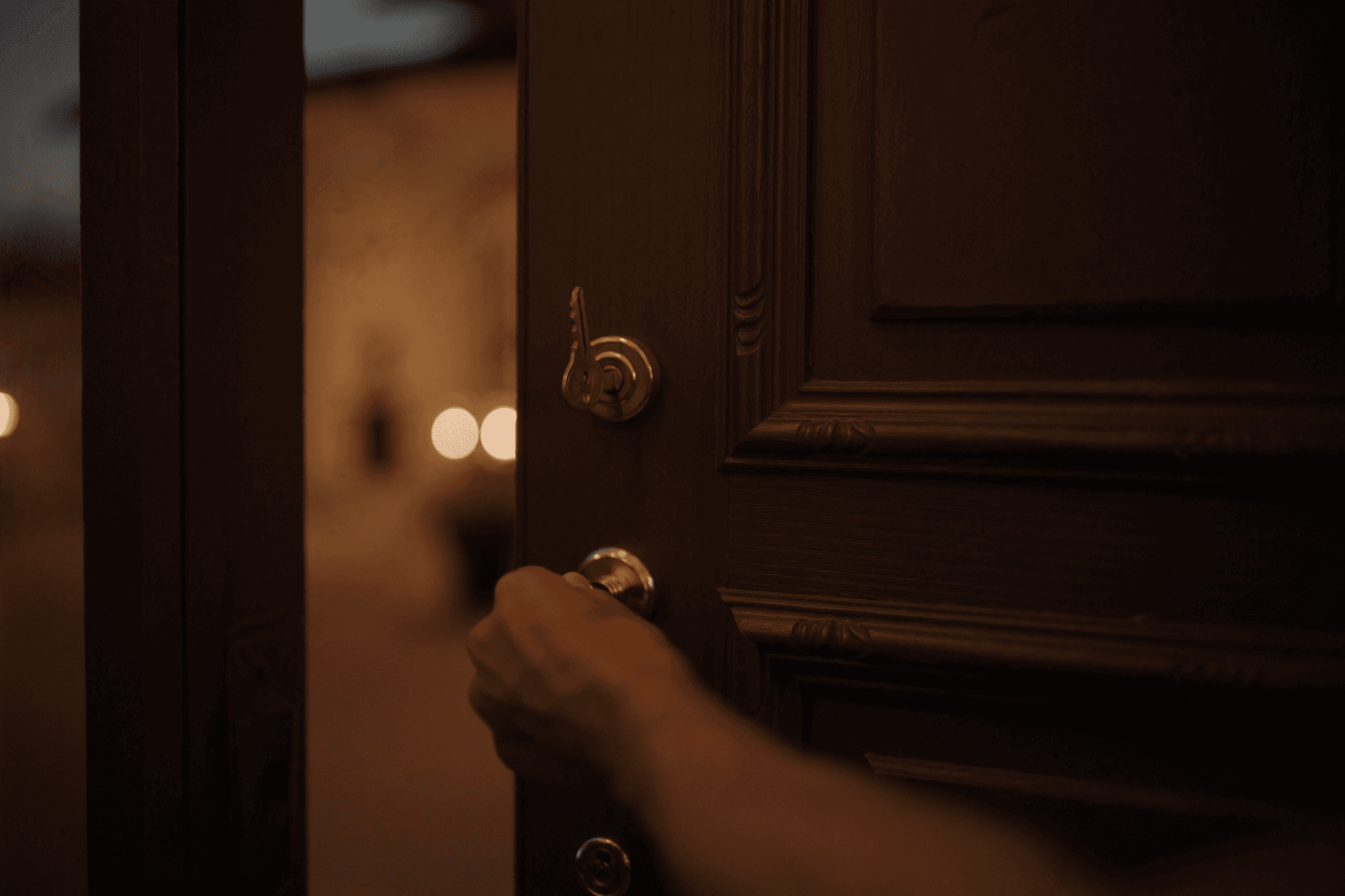 A hand opening the front door of an elegant home at dusk
