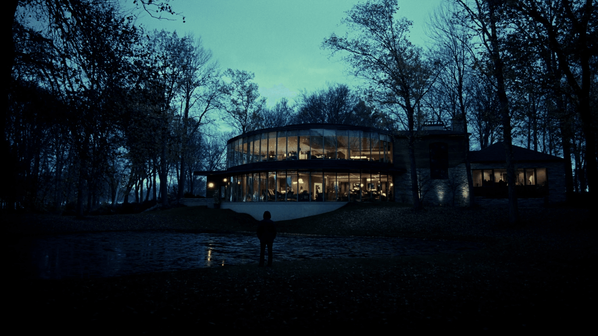 A modern glass home glowing warmly in the woods at dusk